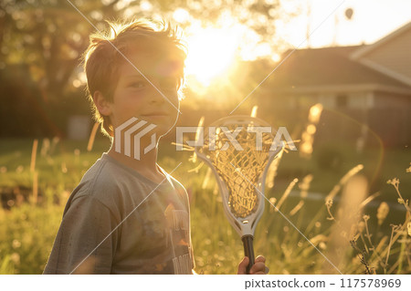 A Young Boy Enjoys a Sunny Afternoon Holding a Lacrosse Stick on a Lush Lawn 117578969