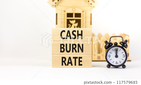 Cash burn rate symbol. Concept words Cash burn rate on wooden blocks on a beautiful white table white background. Black alarm clock, house model. Business cash burn rate concept. Copy space. 117579685