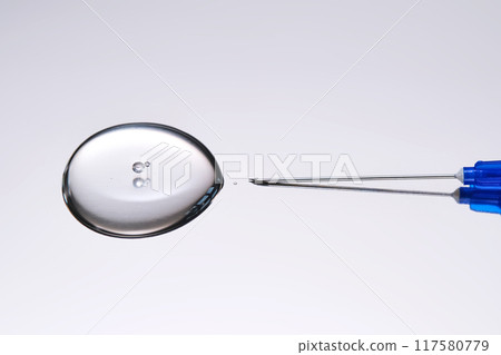 A drop of medicine flowing from a syringe with a needle. 117580779