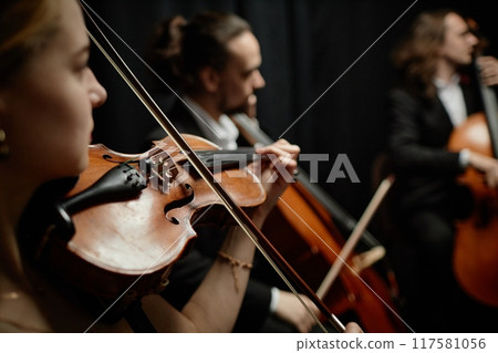 Cropped side view shot of unrecognizable female musician playing violin with chamber quartet on stage, focus on string instrument and bow 117581056