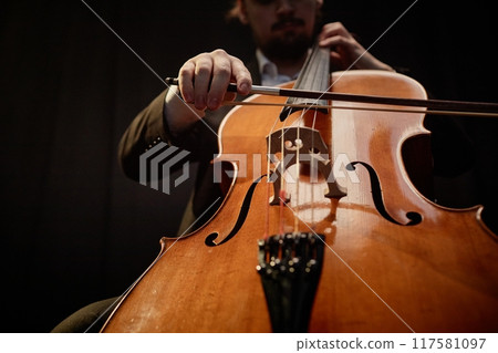 Cropped shot of unrecognizable male cellist performing classical music in dark recording studio with top light, focus on cello 117581097
