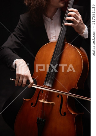 Vertical cropped shot of passionate unrecognizable male musician in black suit playing cello putting on classical music concert in dark studio with dim light Vertical cropped shot of passionate unrecognizable male musician in black suit playing cello putting on classical music concert in dark studio with dim light 117581139