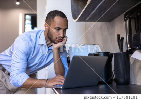 Black guy freelancer standing at kitchen desk reading email message on laptop 117581191
