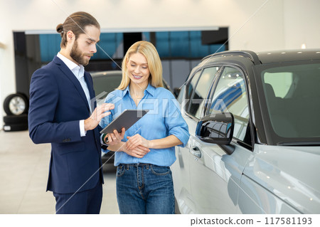 Woman client discussing new luxury vehicle with male consultant at he dealership showroom 117581193