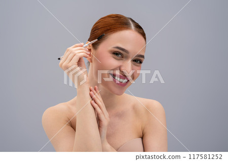 Smiling young girl enhancing her eyebrows with cosmetic brush Smiling young girl enhancing her eyebrows with cosmetic brush 117581252