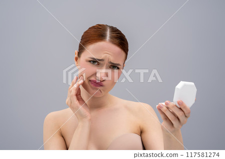 Red-haired lady examining her acne in mirror 117581274