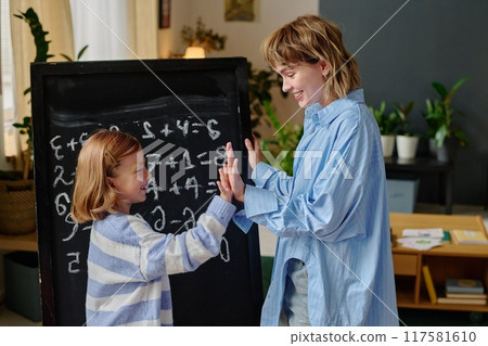 Mom and her lovely brilliant daughter standing next to black board and highing five after math test Mom and her lovely brilliant daughter standing next to black board and highing five after math test 117581610