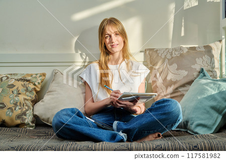 Portrait of female student at home on couch with notebook digital tablet, studying at home 117581982