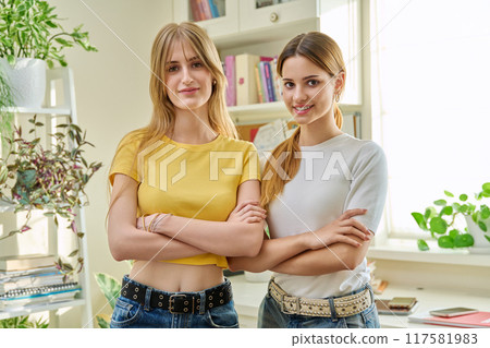 Portrait of two girls positive college students with crossed arms in home 117581983