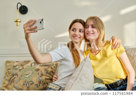 Two cheerful positive teenage girls together at home taking selfie photo 117581984