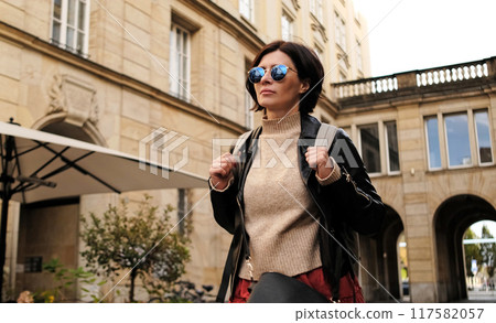 Attractive stylish Woman In Sunglasses Walks By City Street With Backpack 117582057