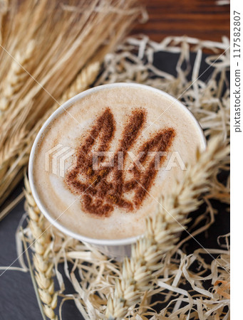 Coffee cup with foam patriotic pattern coat of arms of Ukraine, stencil decor latte mug standing on table with spikelets/ vertical, top view Coffee cup with foam patriotic pattern coat of arms of Ukraine, stencil decor latte mug standing on table with spikelets/ vertical, top view 117582807