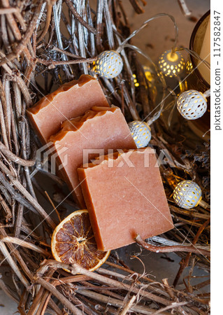 Handmade brown aromatic soap with cinnamon, dried fruits lies cosily on wood with lights. aroma postcard, close-up, vertical 117582847