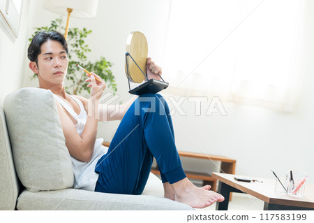 Young man putting on make-up in the living room Young man putting on make-up in the living room 117583199