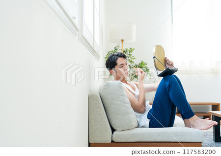 Young man putting on make-up in the living room Young man putting on make-up in the living room 117583200