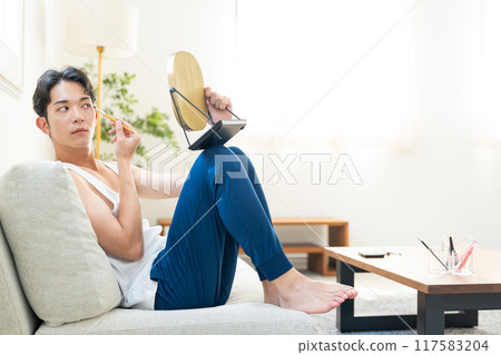 Young man putting on make-up in the living room Young man putting on make-up in the living room 117583204
