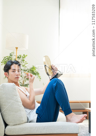 Young man putting on make-up in the living room Young man putting on make-up in the living room 117583209
