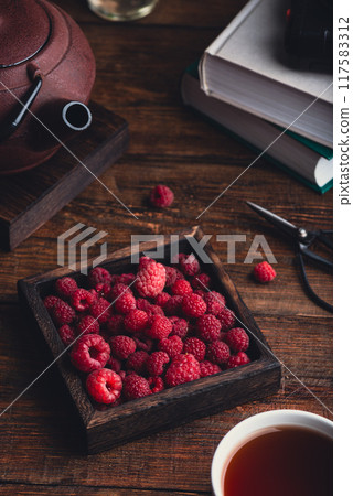 Raspberries and a cup of tea on a table. Raspberries and a cup of tea on a table. 117583312