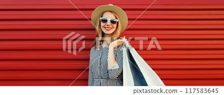 Shopping day, stylish beautiful happy smiling young woman with shopping bags in summer hat on red Shopping day, stylish beautiful happy smiling young woman with shopping bags in summer hat on red 117583645