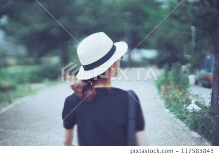Rear view of a woman in a straw hat walking through greenery 117583843