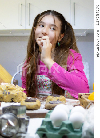 Girl baking cookies in her home kitchen and tasting chocolate with funny face. Girl baking cookies in her home kitchen and tasting chocolate with funny face. 117584570