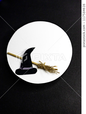 Vertical photo of witch's hat and broom on white circle on dark background. 117584616