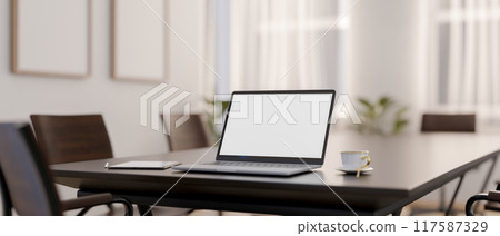 A laptop with a white-screen mockup on a wooden meeting table in a contemporary meeting room. 117587329