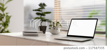 A laptop white-screen mockup on a grey marble table in a contemporary bright room. 117587335