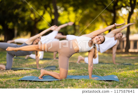 Girl participating in outdoor group yoga session in summer park 117587641