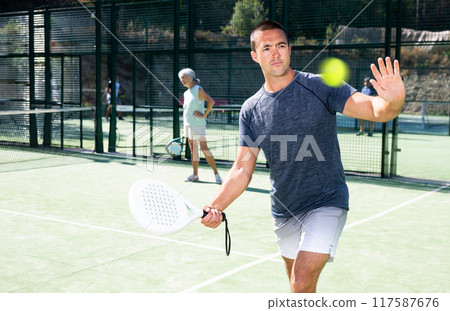 Man swinging racket to hold forehand on open padel tennis court 117587676