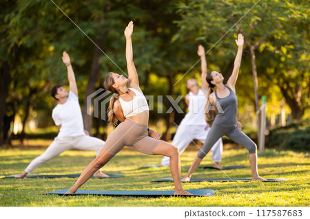 Girl performing Baddha Viparita Virabhadrasana during group yoga 117587683