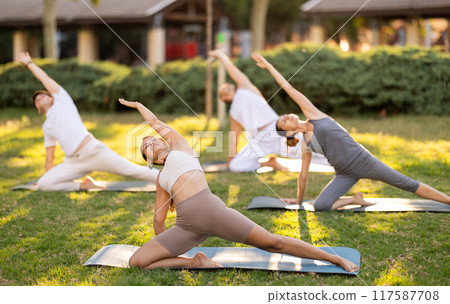 Girl participating in outdoor group yoga session in summer park 117587708