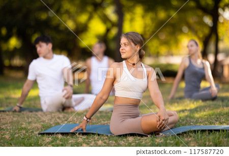Girl performing stretches in lotus position during group yoga outdoors 117587720