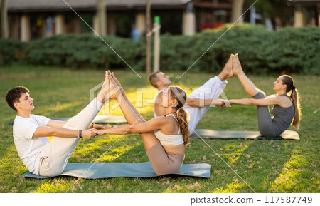 Guy and girl practice pair yoga doing Buddy boat pose asana Guy and girl practice pair yoga doing Buddy boat pose asana 117587749