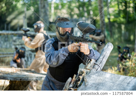 Paintball player in protective uniform aiming and shooting with guns Paintball player in protective uniform aiming and shooting with guns 117587804