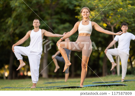 Girl performing one leg balancing pose during outdoor group yoga 117587809