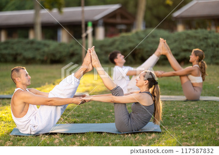 Young couple performing partner Navasana during yoga in park 117587832