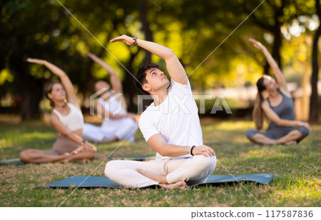 Yoga lesson visitors with guy coach perform padmasana in park 117587836