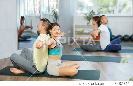 Men and women maintaining healthy lifestyle practicing partner yoga at group lesson 117587845