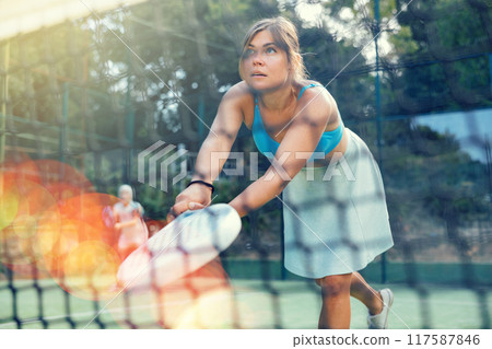 Athletic woman plays padel outdoor. View through tennis net 117587846