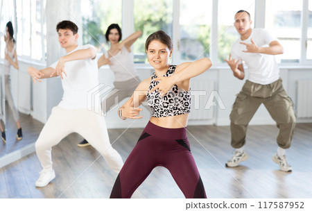 Positive young girl dancing vigorous swing with other people during group training Positive young girl dancing vigorous swing with other people during group training 117587952