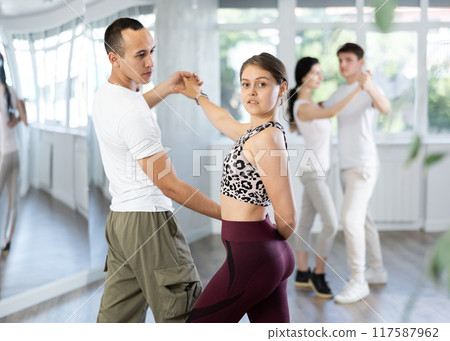 Positive girl dancing playful bachata with partner in studio 117587962