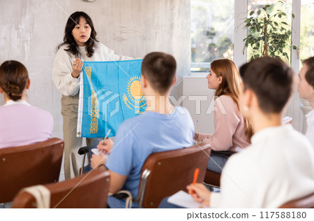 Young woman teacher holding flag of Kazakhstan in front of group of students Young woman teacher holding flag of Kazakhstan in front of group of students 117588180