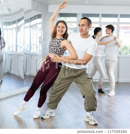 Positive girl dancing playful bachata with partner in studio Positive girl dancing playful bachata with partner in studio 117588260