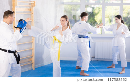 Karate training - woman kicking feet hands in trainer punch mitts in gym Karate training - woman kicking feet hands in trainer punch mitts in gym 117588262