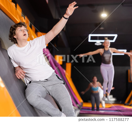 Teenage boy in sport clothes high jumping in trampoline arena 117588277