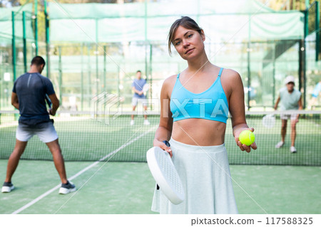 Smiling woman with racket for paddle standing on outdoor tennis court Smiling woman with racket for paddle standing on outdoor tennis court 117588325