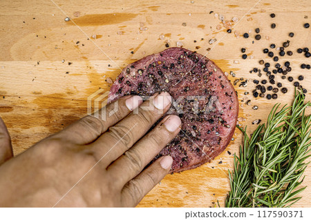A hand is seasoning a tenderloin meat with pepper and salt A hand is seasoning a tenderloin meat with pepper and salt 117590371