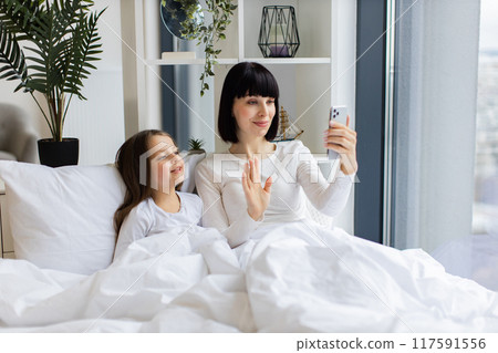 Mom and daughter lying in bed having video call on phone 117591556