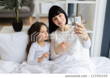 Mom and daughter lying in bed having video call together 117591559